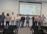 A group of people in front of a screen in a meeting room, smiling into the camera.